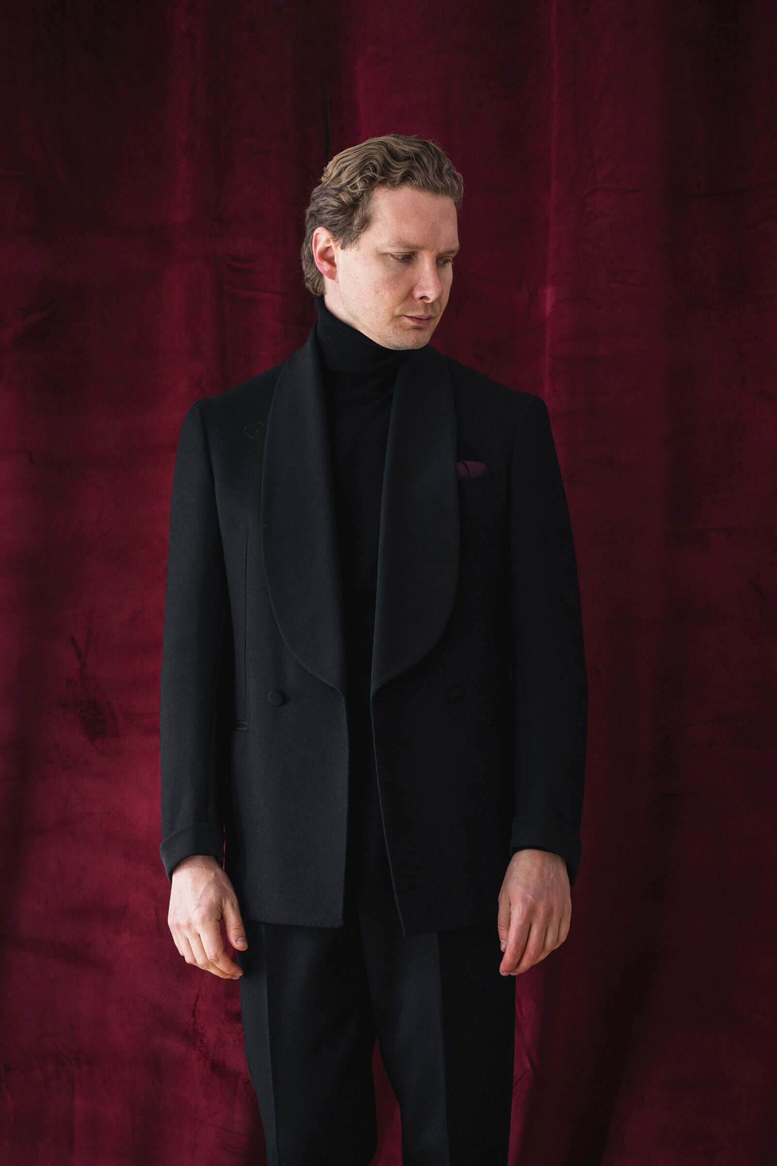 Schwarzes Smokingjackett mit Schalkragen über Rollkragenpullover, bordeauxrotes Einstecktuch